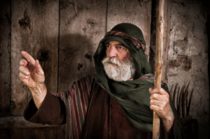 An old man pointing to his right and holding a staff