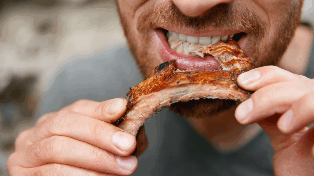 A close-up of a man enjoying a barbecued pork rib, illustrating the common question of should Christians eat pork today.